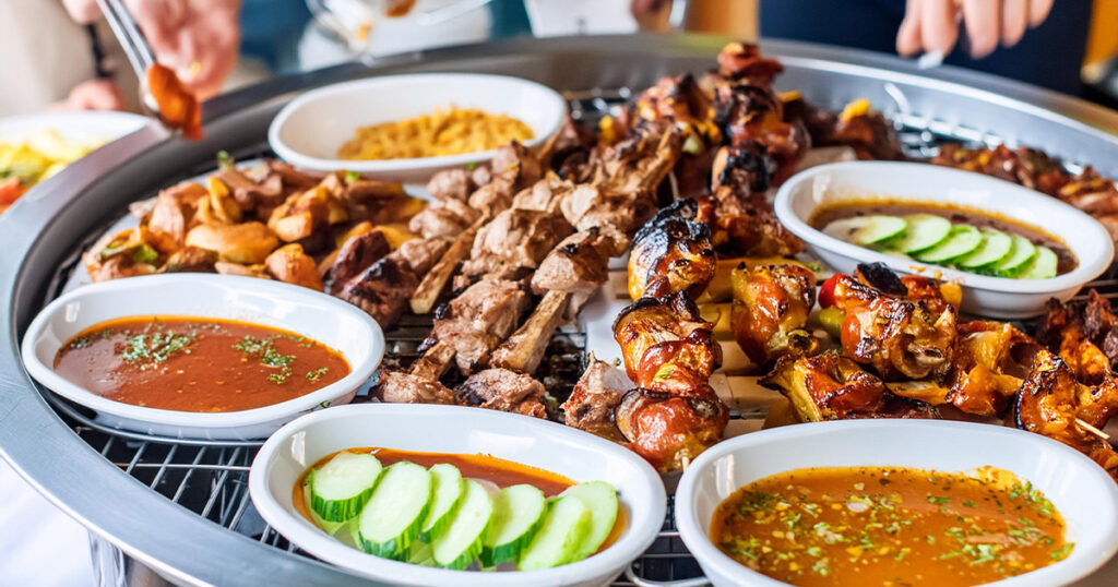 Grillbuffet mit einer Auswahl an gegrilltem Fleisch, Gemüsespießen und Saucen in Schalen